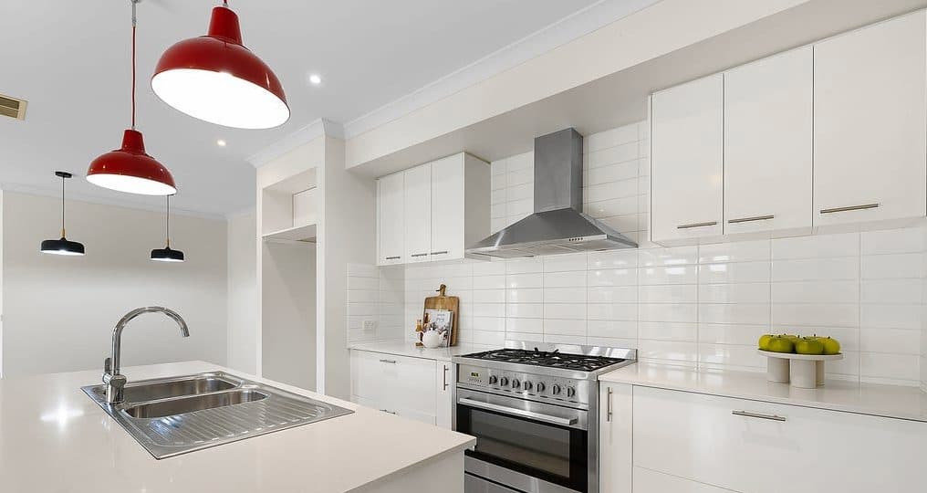 Kitchen styled by Wisteria & Oak in Moama, with red pendant lights over a white stone benchtop
