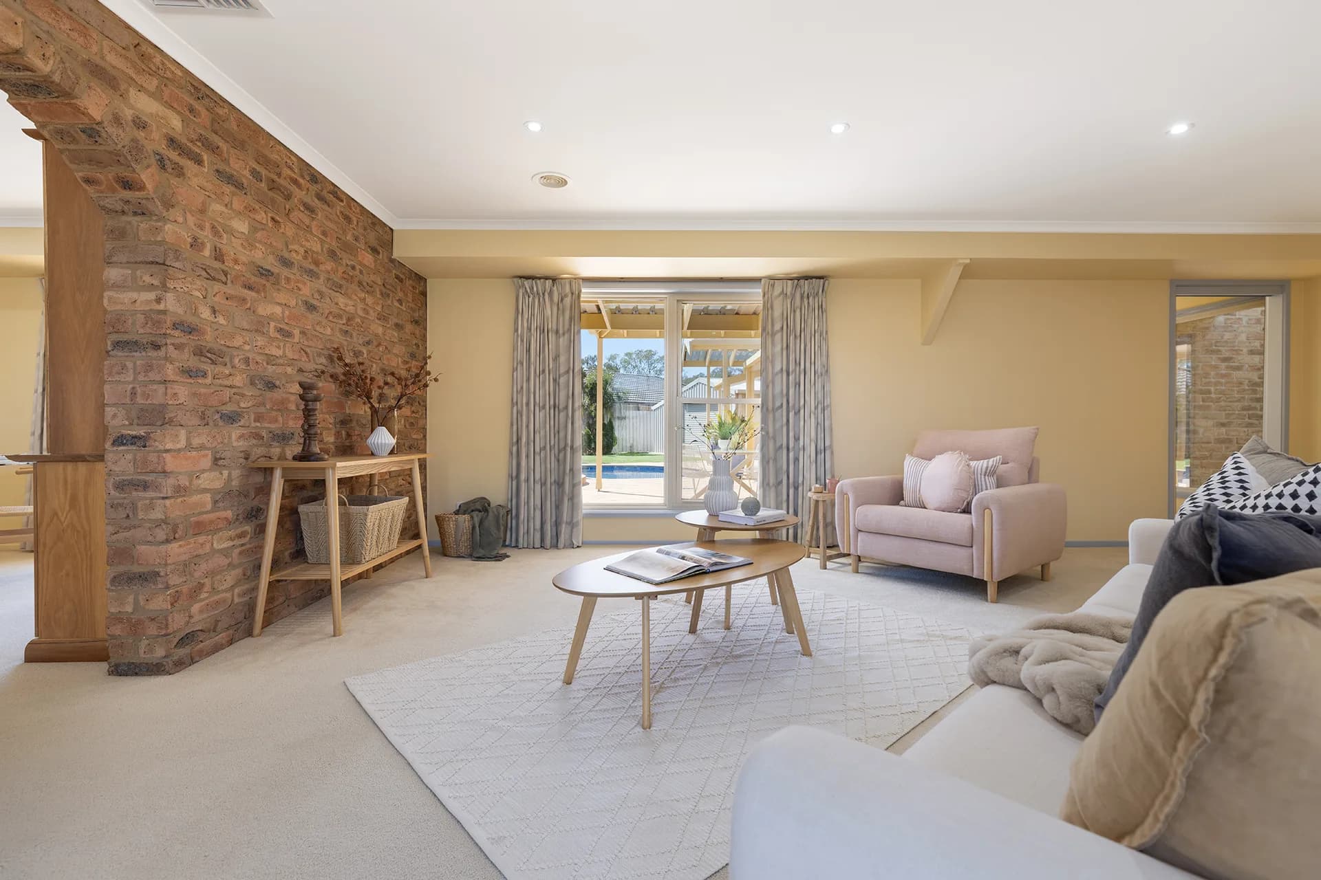 Living room with a brick feature wall, blush armchair and oval timber coffee tables at Rosendale Court, Echuca
